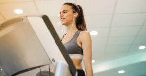 Fit woman running on treadmill in gym wearing sports bra and earphones.
